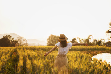 Beautiful and happy asian woman enjoying life in barley field at sunset.