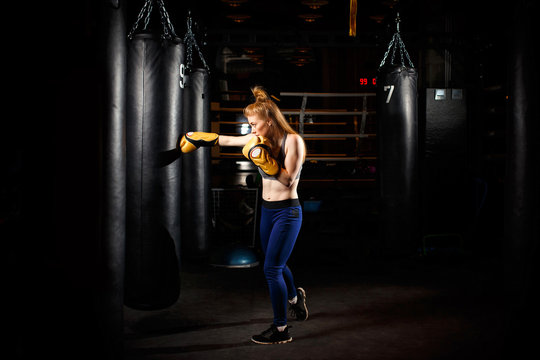 Blonde in boxing gloves trains near black punching bag.