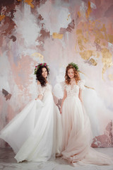 Two charming brides in beautiful spring wreaths on their heads. Beautiful young women in wedding dresses