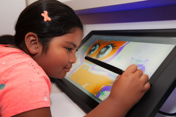 Young girl using a digital pen and drawing tablet to be creative and to make digital art in a...