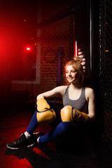 Young athlete woman in boxing gloves sits in ring.