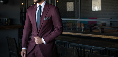 Man in expensive custom tailored suit holding his jacket and posing indoors