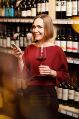 Image of young blonde with glass in hands in store with wine