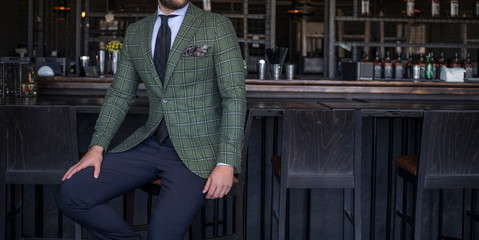 Man in expensive custom tailored suit with green jacket sitting and posing at bar