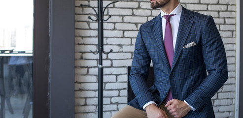 Man in expensive custom tailored suit sitting and posing indoors in front of brick background