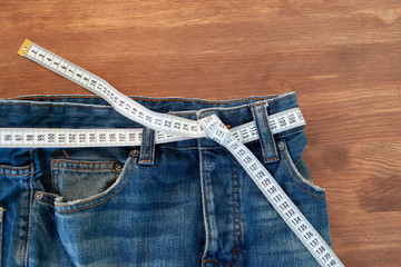 Jeans with a measuring tape on a green background. Weight loss concept 