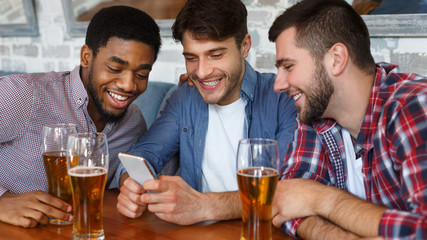Friends meeting in bar, using smartphone and drinking beer