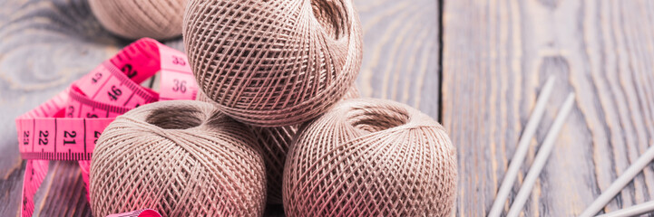 Balls of yarn, knitting needles and measuring tape on a wooden background.