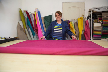 Older woman in a furniture factory is preparing a pink material for measuring and cutting