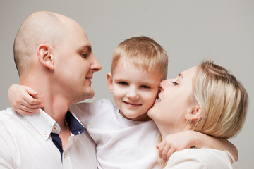 Mom and dad kiss little son. boy is in the center and his parents are around.