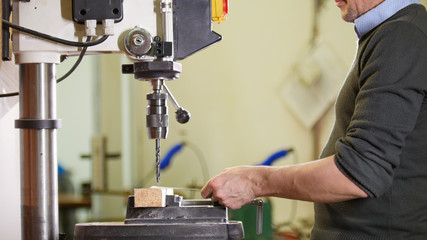 Industrial drilling machine - a man worker makes holes in metal plate
