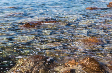 brown stone in close-up, surrounded by sea water to form white foam; rocky coastline