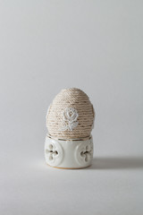 Sur un coquetier en porcelaine trône un oeuf décoré de ficelle et d'une broderie de coton