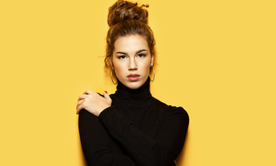 Portrait of georgeous girl posing for fashion photoshoot on yellow background. Pretty model dressed in stylish black pullover. Trend and lifestyle concept