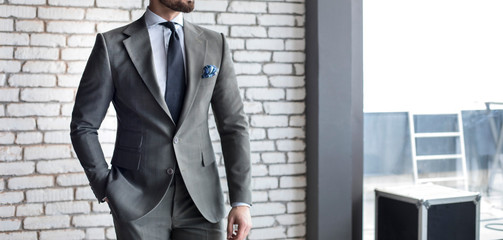 Man in expensive custom tailored suit standing and posing indoors in front of brick wall background