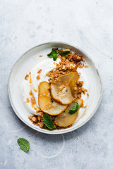 Greek yogurt with caramelized pear, granola, nuts and melted sugar for a wholesome breakfast on a gray ceramic plate. Rustic style. Top view.