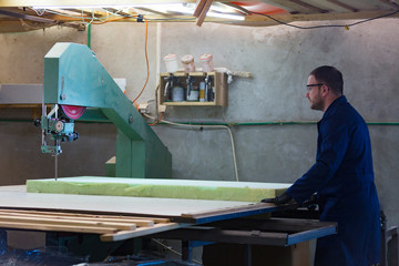 Young man in a furniture factory is cutting the foam for the sofa
