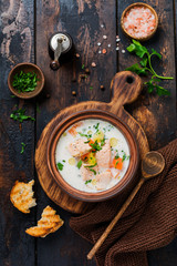 Warm Finnish creamy soup with salmon and vegetables in old ceramic bowl on old wooden background. Rustic style. Top view.