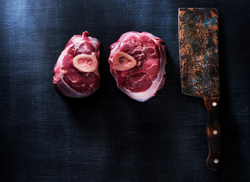 Raw Osso buco Veal shanks and meat cleaver on dark background and copy space for the recipe, top view