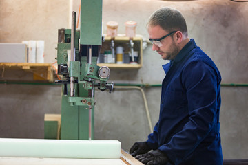 Portrait of a young man in a furniture factory cutting the foam for the sofa