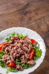 Tuna salad with arugula and tomatoes in white plate on wooden table background