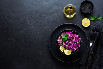 Salad of purple Peking cabbage with olive oil, lime and black sesame seeds in ceramic plate on dark concrete background.