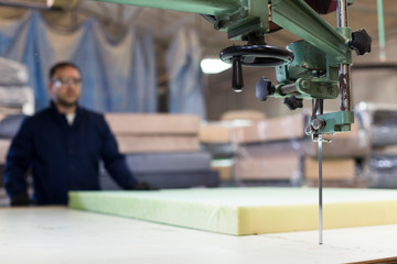 Young man in a furniture factory is cutting the foam for the sofa