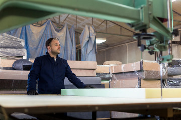 Fototapeta na wymiar Young man in a furniture factory is cutting the foam for the sofa