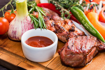 Close up roasted pork neck with spices, vegetables and ketchup on wooden board