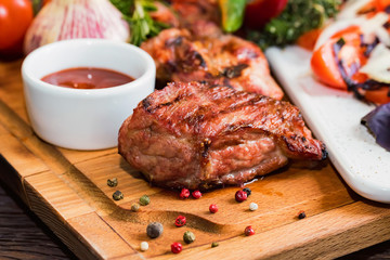 Close up roasted pork neck with spices, vegetables and ketchup on wooden board