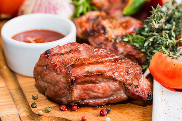 Close up roasted pork neck with spices, vegetables and ketchup on wooden board