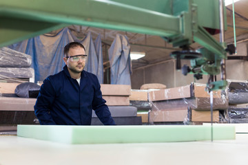 Fototapeta na wymiar Young man in a furniture factory is cutting the foam for the sofa