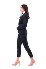 Profile view of successful female ceo in black suit walking and looking forward. Full body isolated on white background.