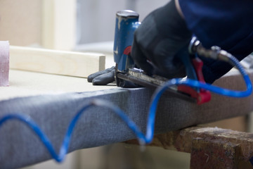 Closeup of a young man in a furniture factory who puts together one part of the sofa with a stapler