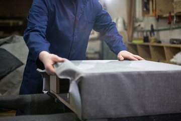 Closeup of a young man in a furniture factory who puts together one part of the sofa