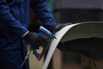 Closeup of a young man in a furniture factory who puts together one part of the sofa with a stapler