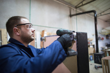 Young man in a furniture factory attaches the sofa leg