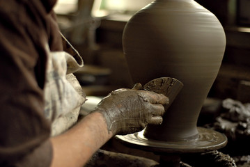 The man carves an ornament on an earthenware bowl. Handmade products on the table at home workshop.