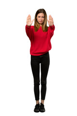 Obraz na płótnie Canvas A full-length shot of a Young woman with red sweater making stop gesture and disappointed over isolated white background