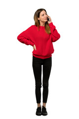 Fototapeta premium A full-length shot of a Young woman with red sweater keeping a conversation with the mobile phone over isolated white background