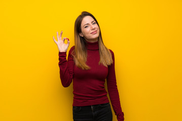 Woman with turtleneck over yellow wall showing ok sign with fingers