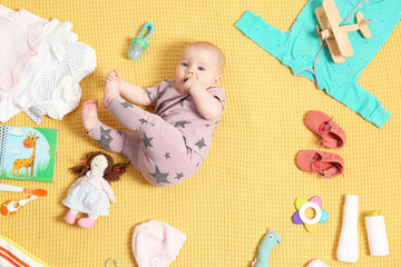 Cute little baby with clothing and accessories on color blanket, top view