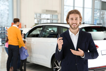 Car salesman with key and blurred family near auto on background