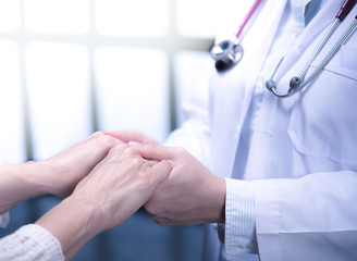Medical doctor reassuring patient by holding patient’s hands in hospital setting