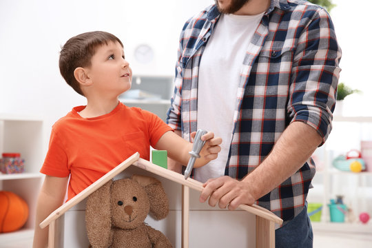 Man And His Child Playing Builders With Wooden Doll House At Home