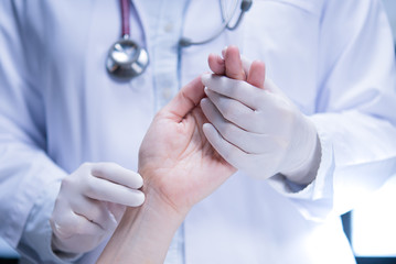 Medical doctor wearing latex gloves examining patient’s pulse in hospital setting