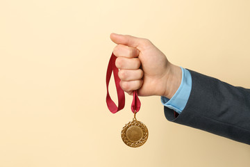 Fototapeta na wymiar Man holding golden medal on color background, closeup. Space for text