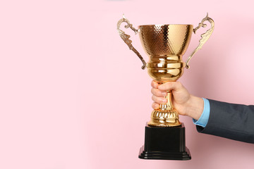 Man holding golden trophy cup on color background, closeup. Space for text