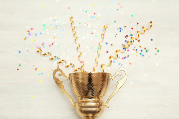 Golden trophy cup and streamers on wooden background, top view