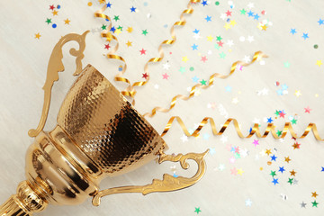 Golden trophy cup with streamers on wooden background. Space for text